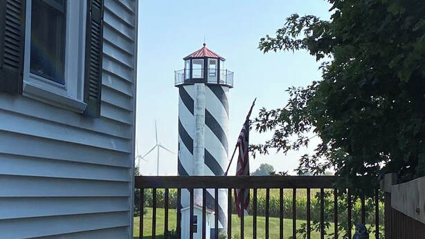 A wooden deck with a view of a lighthouse and wind turbines in the background.