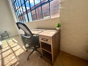 A corner office with a large window, a desk, a chair, and a small plant.