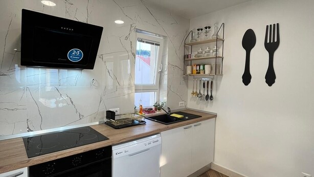 A modern kitchen with a built-in oven, dishwasher, and a flat-screen TV mounted on the wall. - New modern 3-bedroom apartment with AC in Supetar (Selca)