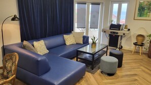 A modern living room with a blue sofa, a glass coffee table, a small ottoman, a lamp, a chair, and a grill. - New modern 3-bedroom apartment with AC in Supetar (Selca)