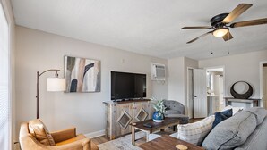 A living room with a sofa, a coffee table, a TV, and a ceiling fan. - Cottage 2 - Bourbon Way (Ridgeland)