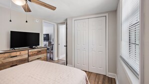 A bedroom with a bed, a TV on a wooden dresser, a ceiling fan, and a closet. - Cottage 2 - Bourbon Way (Ridgeland)