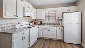 A kitchen with white cabinets, a stove, a sink, and a refrigerator. - Cottage 2 - Bourbon Way (Ridgeland)