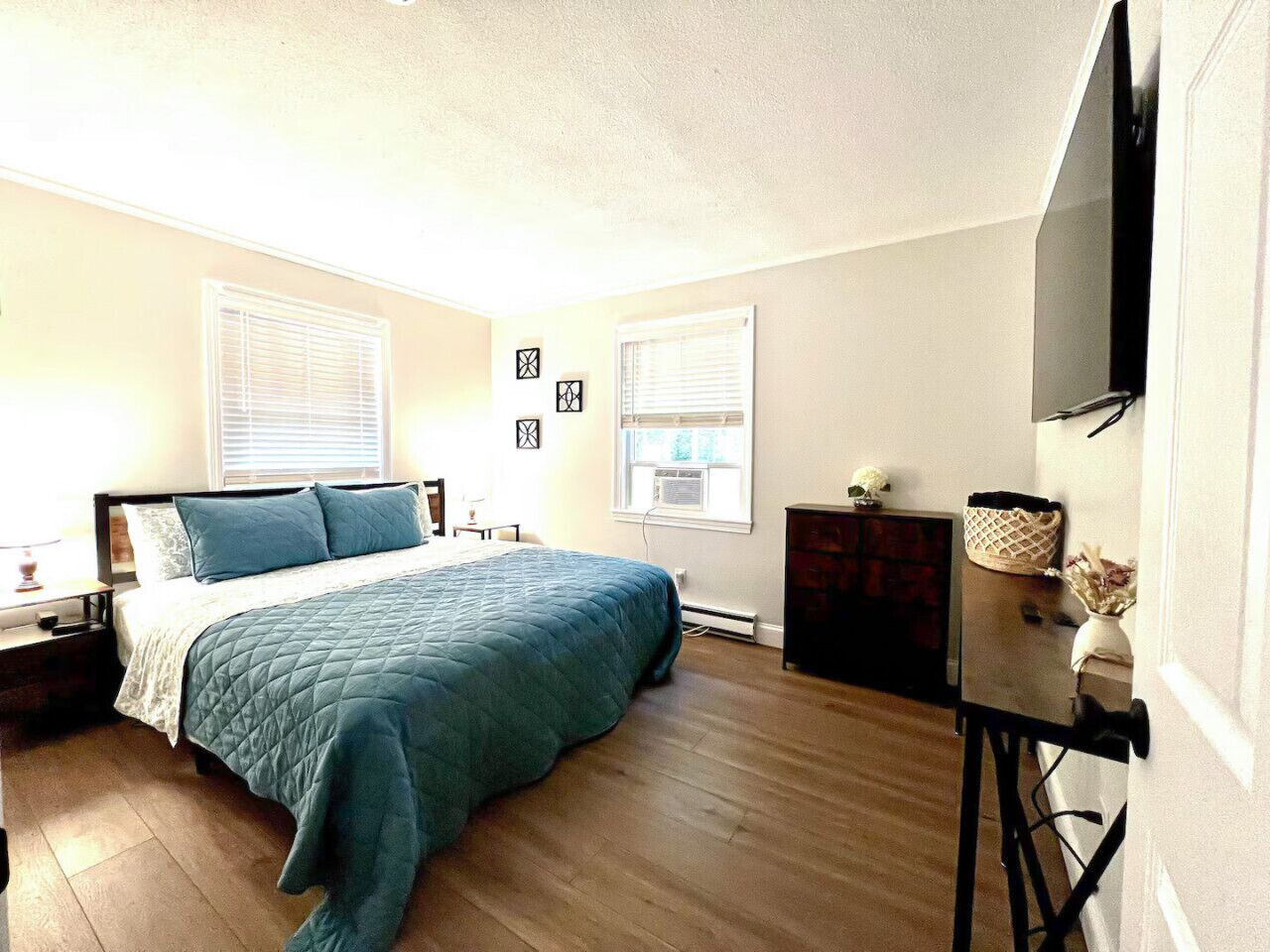 A bedroom with a bed, a dresser, a TV, and a window with blinds.