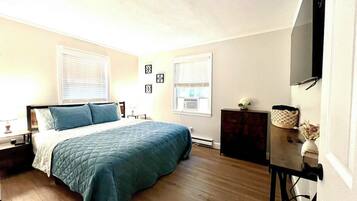 A bedroom with a bed, a dresser, a TV, and a window with blinds.