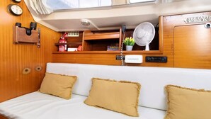 L’intérieur chaleureux d’un chalet avec un banc rembourré blanc, des coussins beige, un petit ventilateur, un extincteur et un mur recouvert de panneaux en bois.