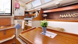 Un petit espace cuisine avec des placards en bois, un évier et un petit plan de travail. Une plante en pot est posée sur le plan de travail, et le nom « NAMAST » est visible sur le mur.