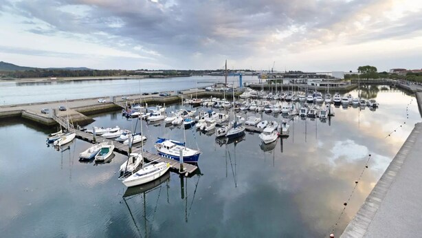 Un port de plaisance où de nombreux bateaux sont amarrés, un pont en arrière-plan et une eau calme qui reflète le ciel.