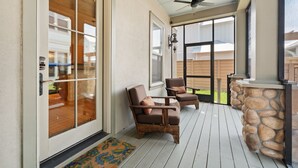 Eine überdachte Veranda mit zwei braunen Ledersesseln, einer Steinbar und einem Deckenventilator.