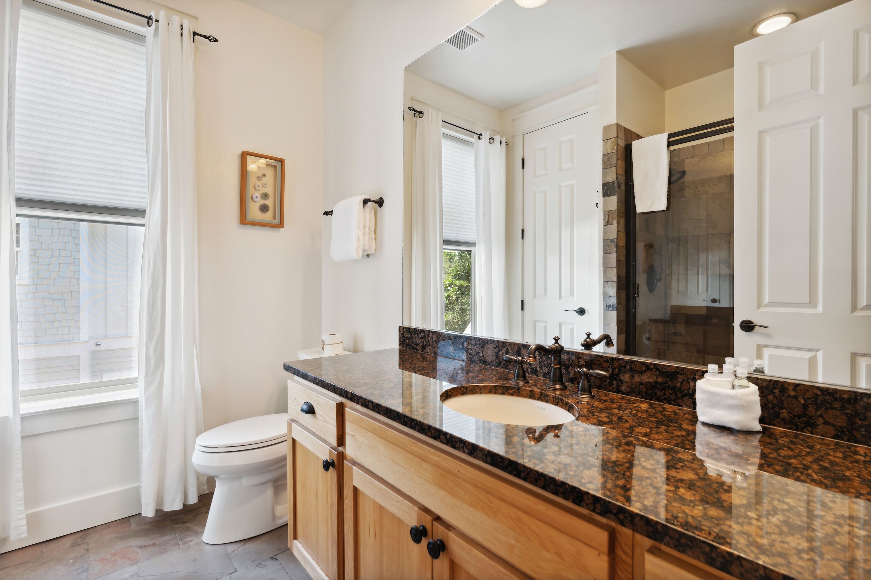 Un bagno con un water bianco, un lavabo con piano in granito, armadietti in legno e uno specchio grande.
