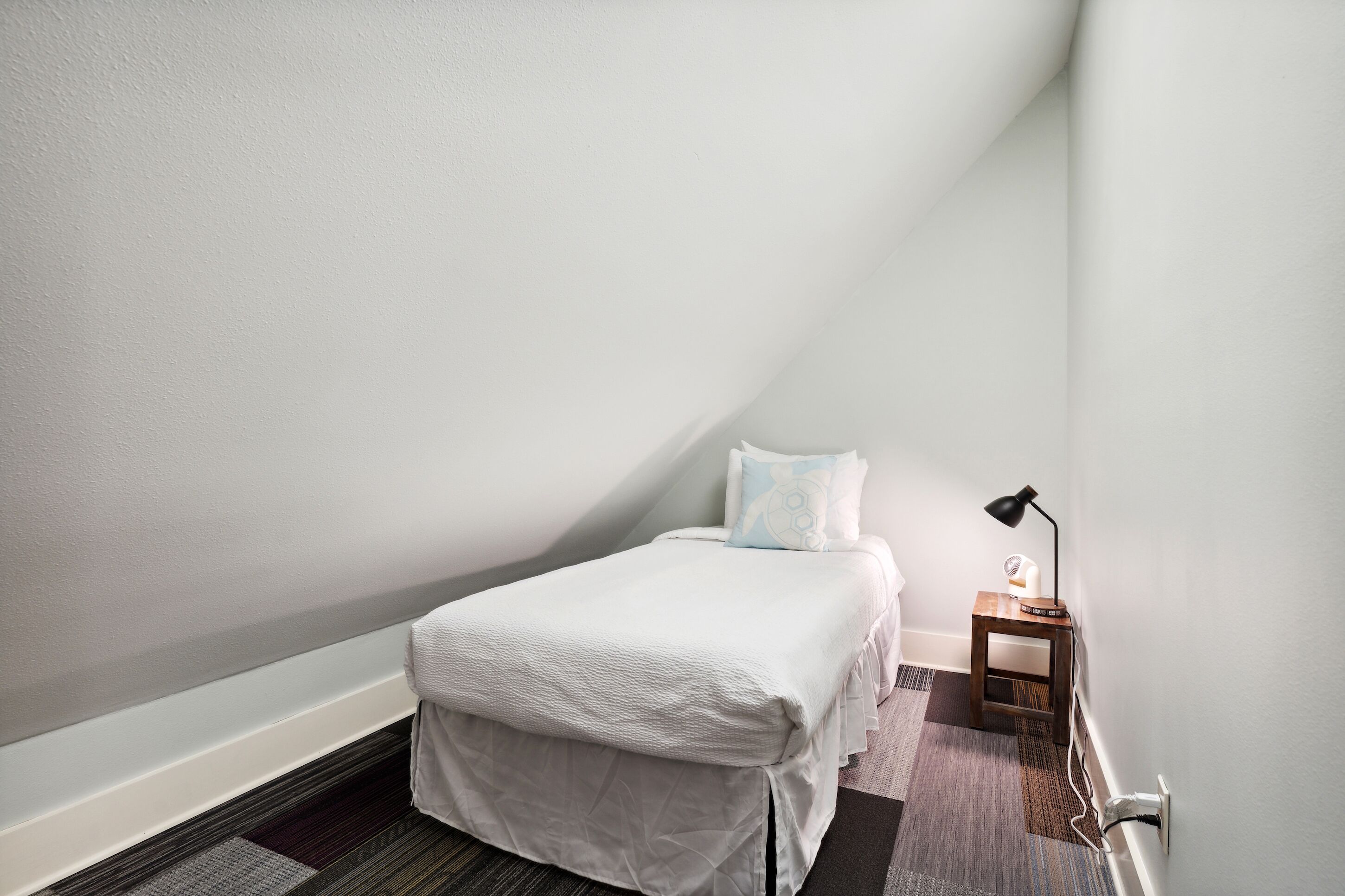 Ein kleines, ordentlich eingerichtetes Schlafzimmer mit einem Einzelbett, einem Nachttisch, einer Lampe und einer Heizung.