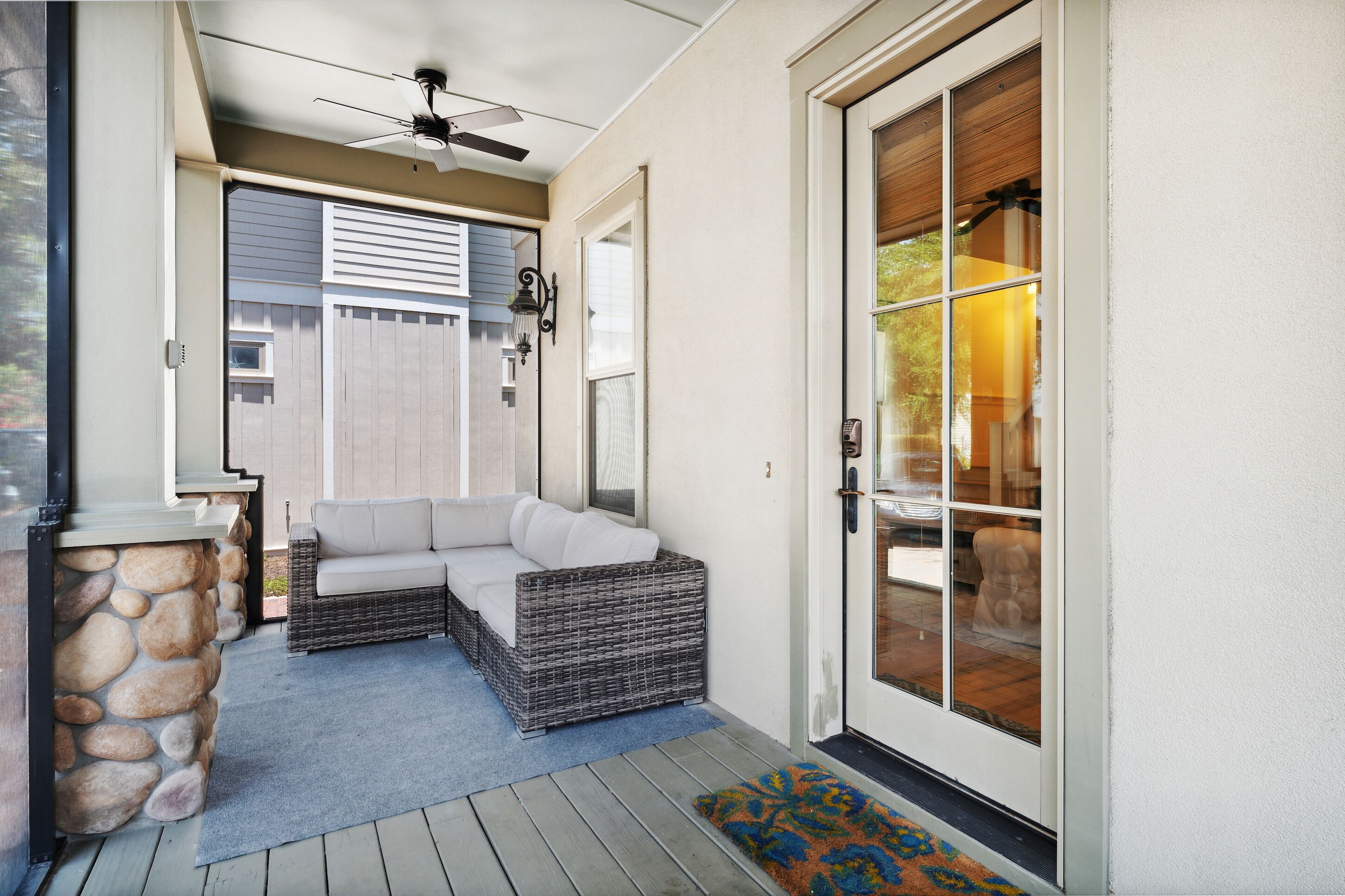 A covered porch with a stone wall, a wicker sofa, and a ceiling fan.