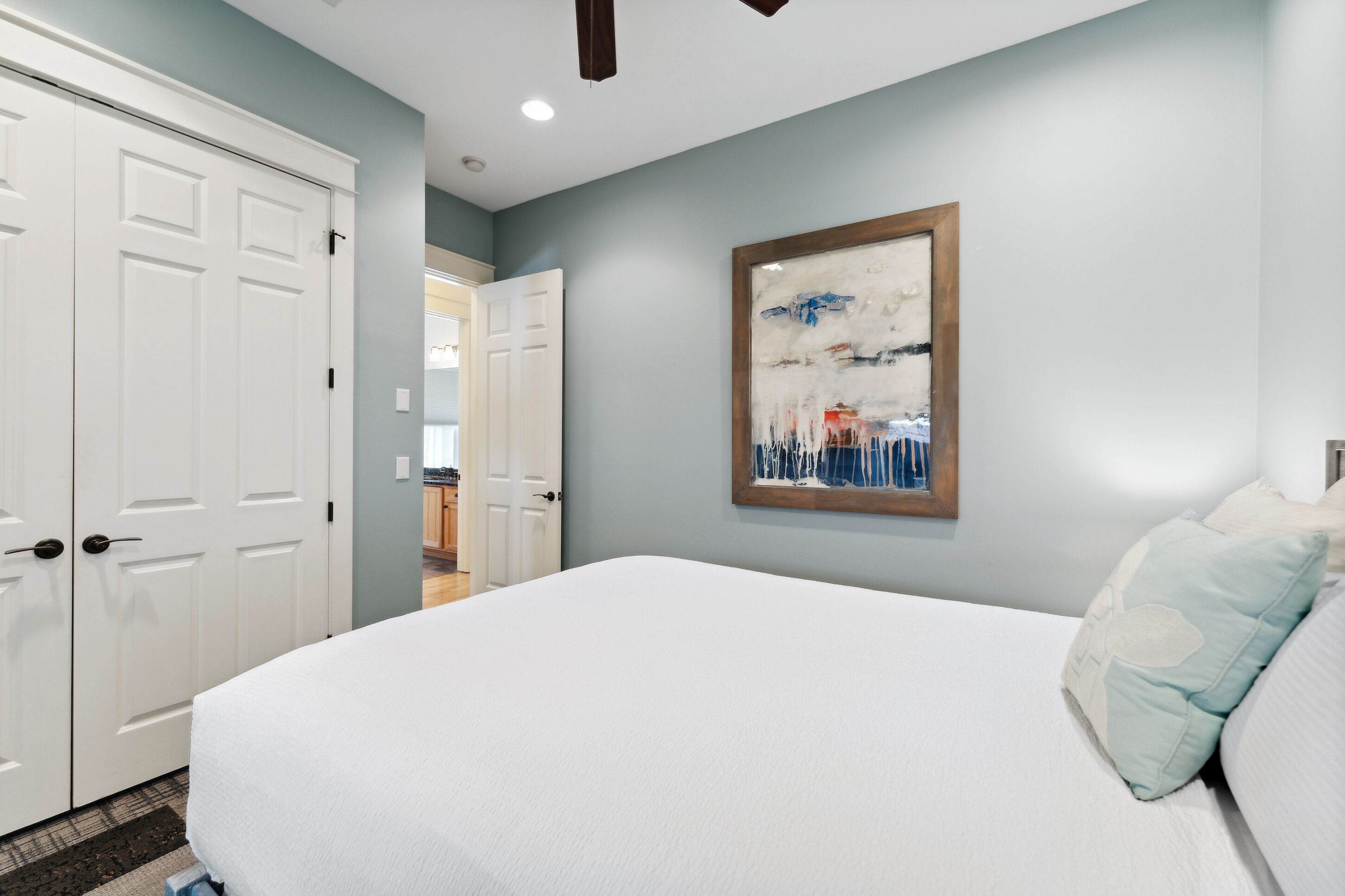 A bedroom with a large bed, white walls, and a painting.