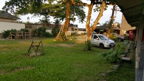 Patio trasero con un coche estacionado bajo un árbol, una escalera y un pequeño jardín.