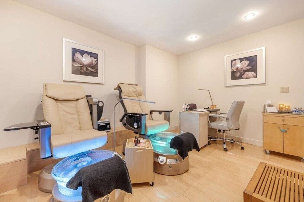 A modern spa room with a massage chair, a foot bath, and a desk with a computer.