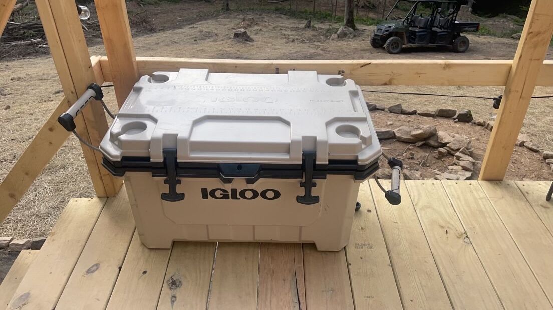 A large, beige IGLOO storage box with a handle and latch, placed on a wooden deck.