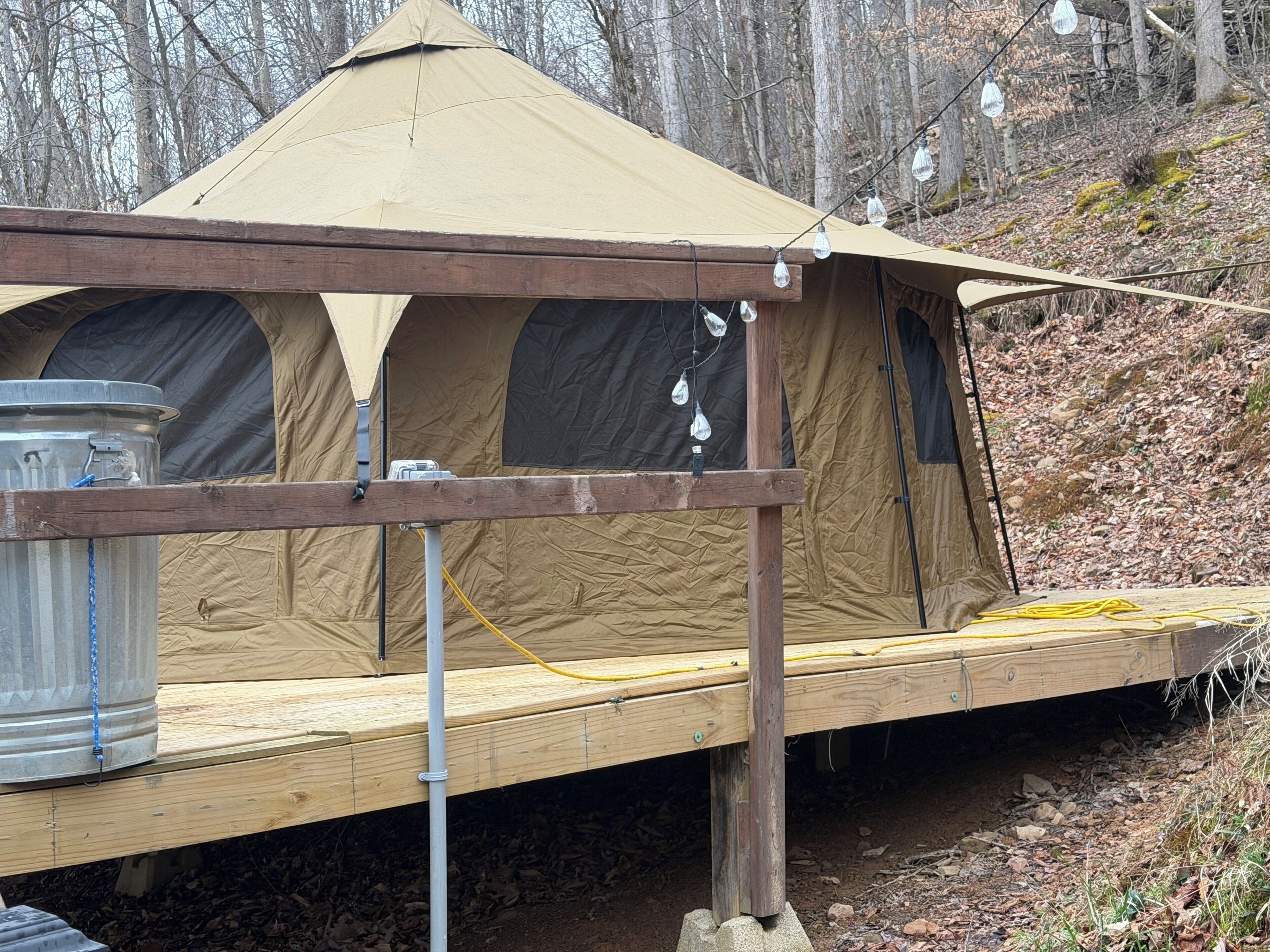 A tent with a wooden platform, a metal barrel, and a yellow hose.