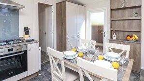 Une cuisine moderne équipée d’une cuisinière à gaz, d’un four et d’un meuble en bois. On y trouve une table à manger mise avec des assiettes, des verres et un panier de fruits.