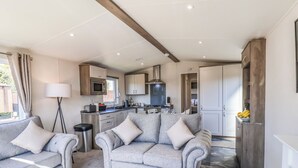 Un salon moderne avec des canapés gris et une table basse, une cuisine avec des meubles blancs et une cuisinière, et un coin repas avec une table et des chaises.