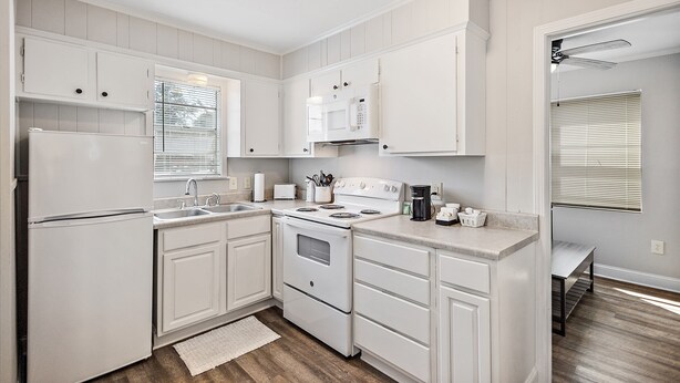A kitchen with white cabinets, a stove, a microwave, and a sink. - Cottage 4 - Nobody Inn (Ridgeland)