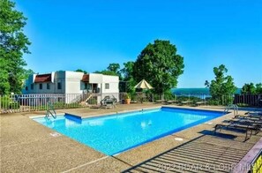 Relax by the pool surrounded by lush greenery and a wooden deck.