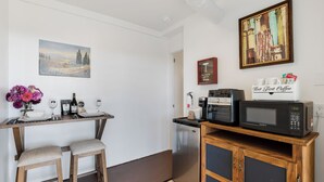 Een kleine keuken met een eethoek, een magnetron, een koffieapparaat en een kleine koelkast.