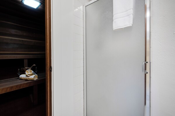 A shower area with a glass door, a bench with towels, and a wooden ceiling.