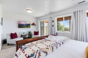 A bedroom with a large bed, a chair, a small table, and a painting on the wall.