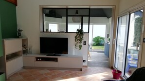 A modern living room with a flat-screen TV, a coffee table, and a sliding glass door leading to a balcony. - House in quiet, comfortable neighbourhood, close to town center and shops (Vannes)