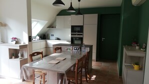 A kitchen with a dining table, chairs, and pendant lights. There is a green wall and a door in the background. - House in quiet, comfortable neighbourhood, close to town center and shops (Vannes)