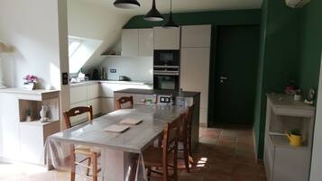 Een keuken met een eettafel, stoelen en hanglampen. Achtergrond is een groene muur en een deur.