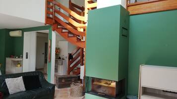 Een woonkamer met een groene wand, een houten trap, een open haard en een bank.
