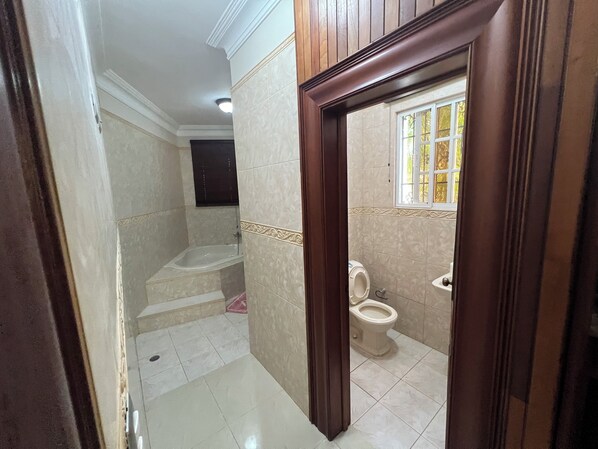 A bathroom with a bathtub, toilet, and sink, featuring tiled walls and a wooden door frame.