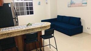 Et køkken med en bordplade i granit, et køleskab og en blå sofa i opholdsstuen.