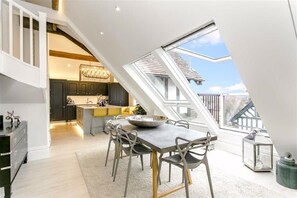 A dining area with a high ceiling and skylight, a kitchen with dark cabinets, and a view of the outside.