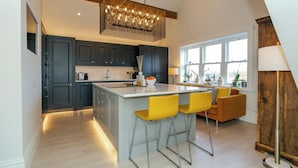 A modern kitchen with dark cabinets, a central island with bar stools, and a large window providing natural light. - Executive 3 bedroom Penthouse apartment, 2 bath and Mezzanine (Harrogate)