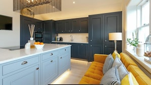 A modern kitchen with dark cabinets, a large island, and a yellow sofa by the window. - Executive 3 bedroom Penthouse apartment, 2 bath and Mezzanine (Harrogate)