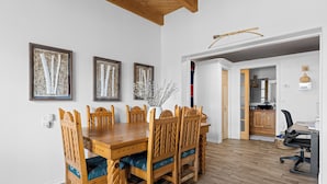A dining area with a wooden table and chairs, framed artwork on the wall, and a kitchen visible through an open doorway. - Bosque "Abeyta" Casita (Bosque)