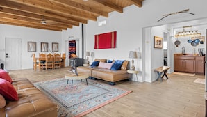 A spacious living room with a wooden ceiling, a sofa set, a dining table, and a kitchen area with hanging pots. - Bosque "Abeyta" Casita (Bosque)