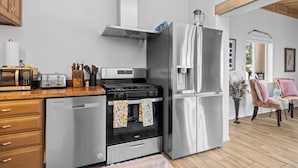 A modern kitchen with stainless steel appliances, wooden cabinets, and a dining area with chairs. - Bosque "Abeyta" Casita (Bosque)