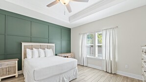 Un dormitorio con cama, mesitas de noche, cómoda, ventilador de techo y ventana con cortinas.