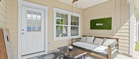A covered porch with a ceiling fan, a white door, a window, a sofa, and a small table.