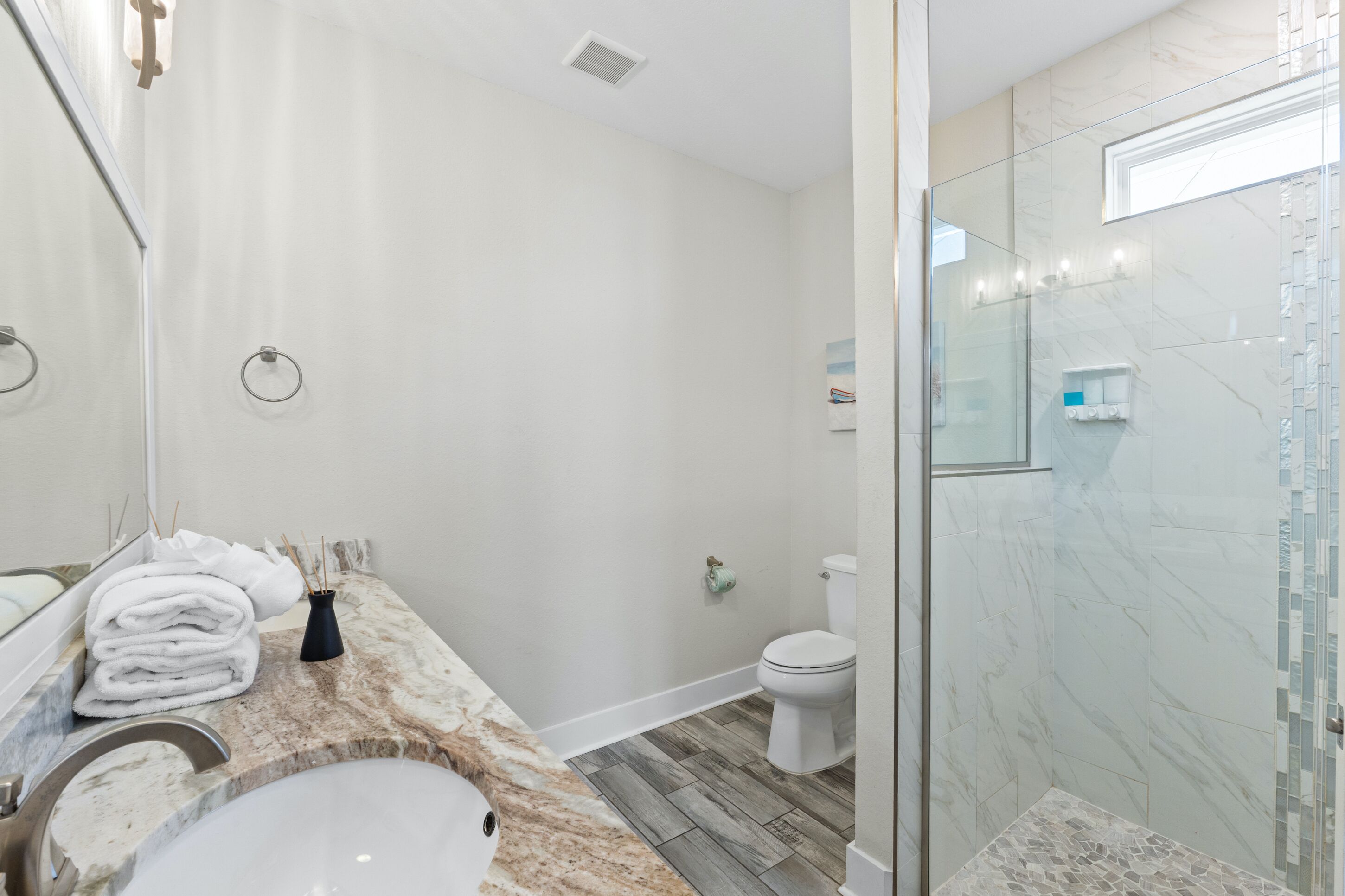 Un baño moderno con encimera de mármol, ducha con cerramiento de vidrio y retrete.