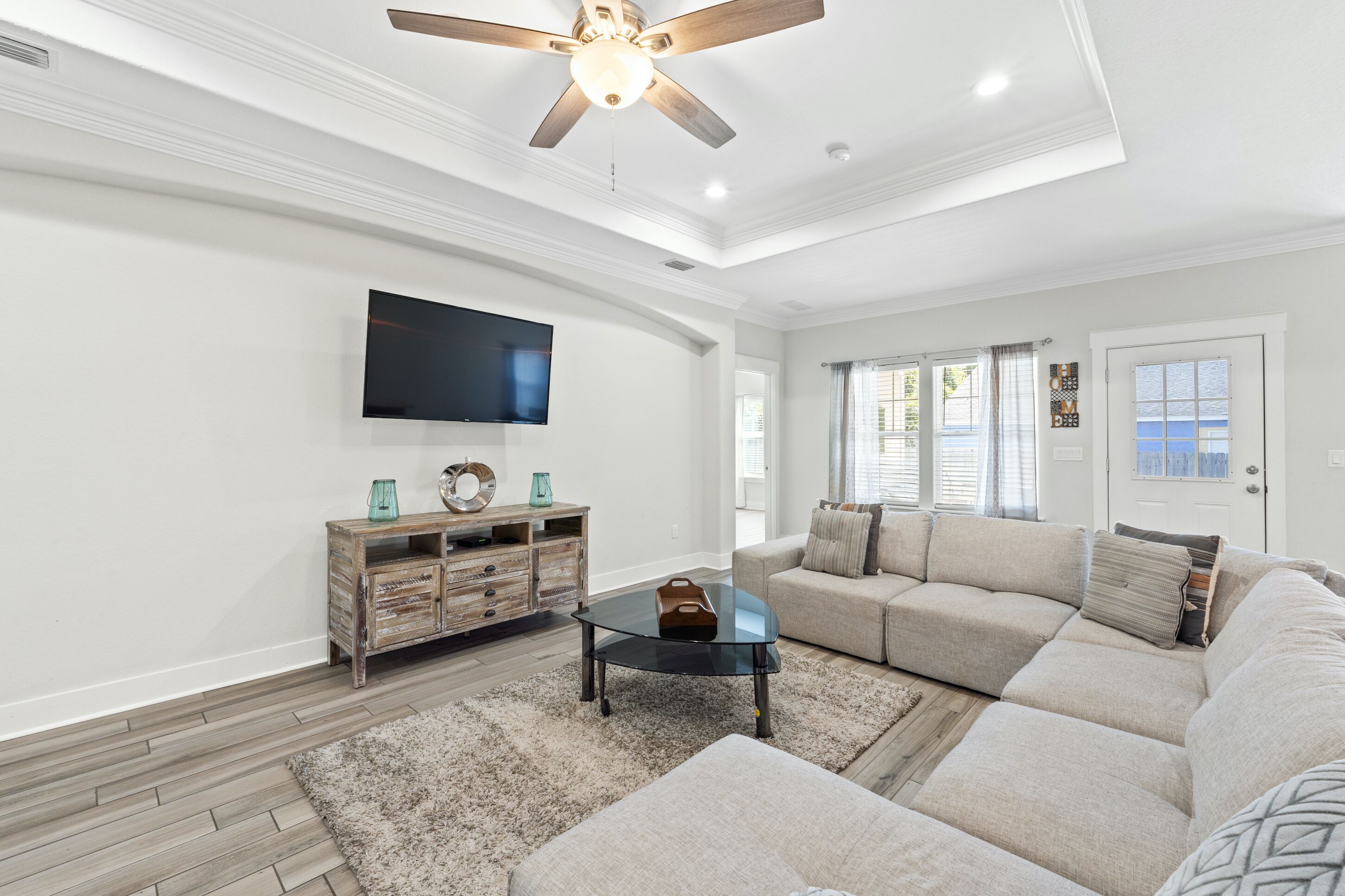 A spacious living room with a sectional sofa, a coffee table, and a flat-screen TV mounted on the wall.