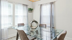 Un comedor con una mesa de vidrio, cuatro sillas y una araña.