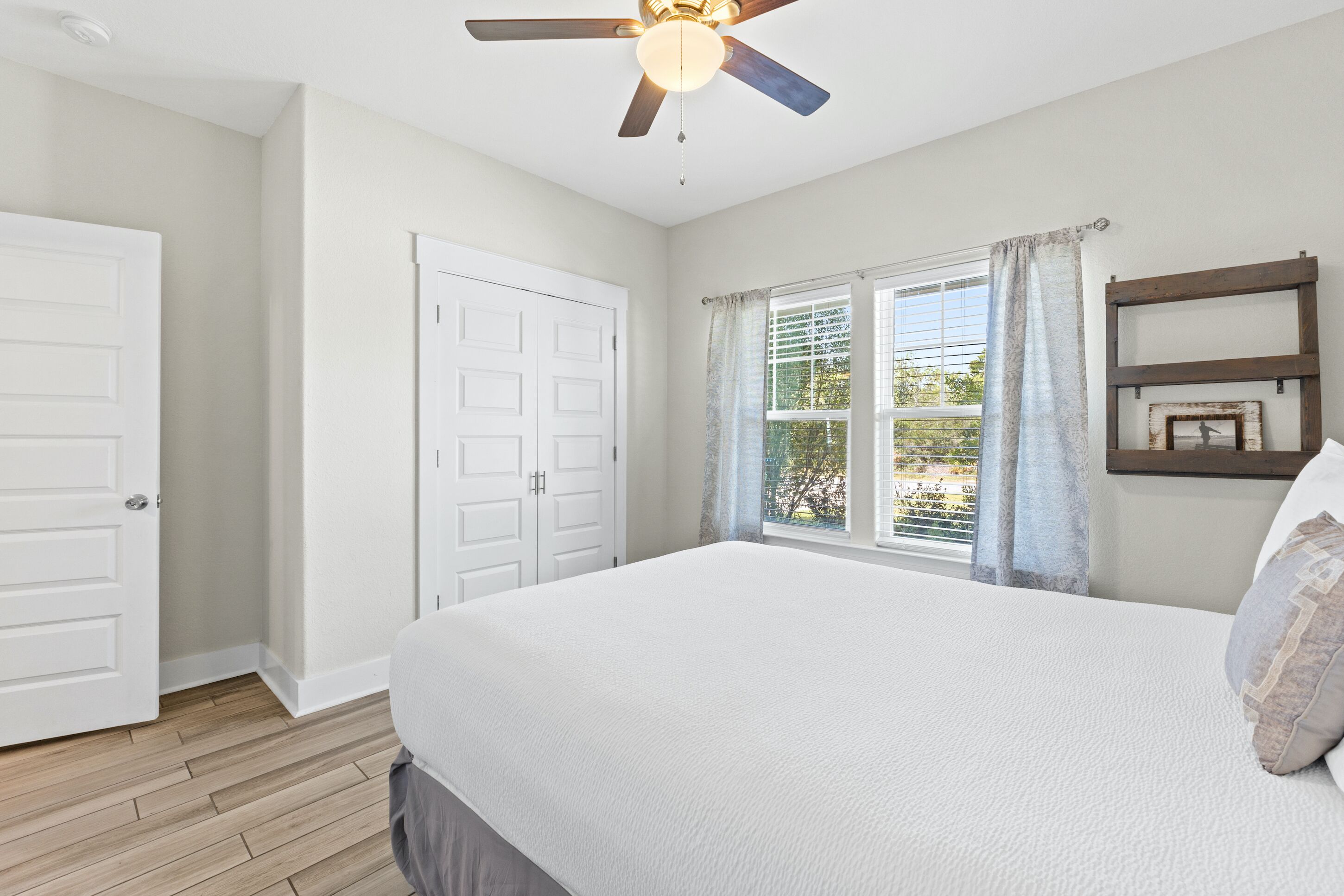A bedroom with a large bed, a ceiling fan, a window with curtains, and a door.