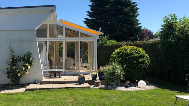 A modern house with a glass conservatory, a well-maintained lawn, and a large tree in the background.