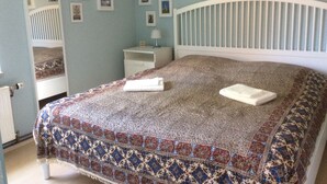 A bedroom with a patterned bedspread, a white headboard, a bedside table with a lamp, and a wall with framed pictures.