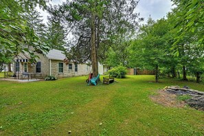 A stone house with a grassy yard, a wooden bench, and a wheelbarrow.
