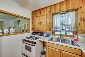 A kitchen with wooden cabinets, a stove, a sink, and a window with curtains.